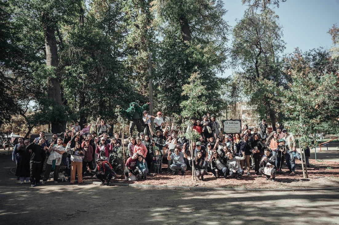 Un grupo numeroso de personas reunidas bajo los árboles del parque.